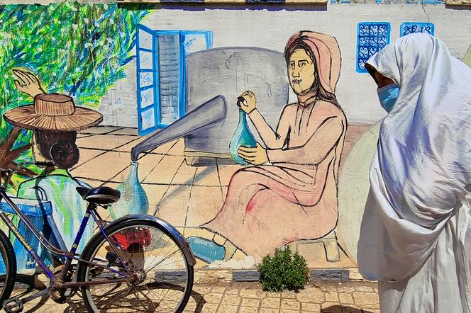 Une femme en habit traditionnel tunisien passe devant une fresque représentant une scène de distillation, à Nabeul, en avril 2021.