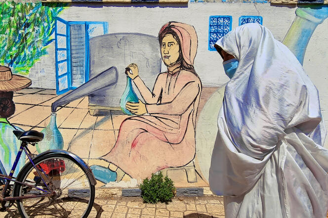 Une femme en habit traditionnel tunisien passe devant une fresque représentant une scène de distillation, à Nabeul (Tunisie), en avril.