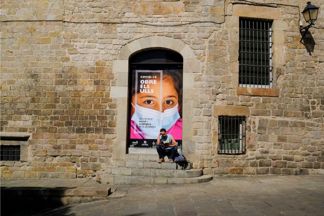 Un homme lit un livre sous un poster « COVID-19, ouvrez les yeux » à Barcelone (Espagne), le 19 avril 2021.
