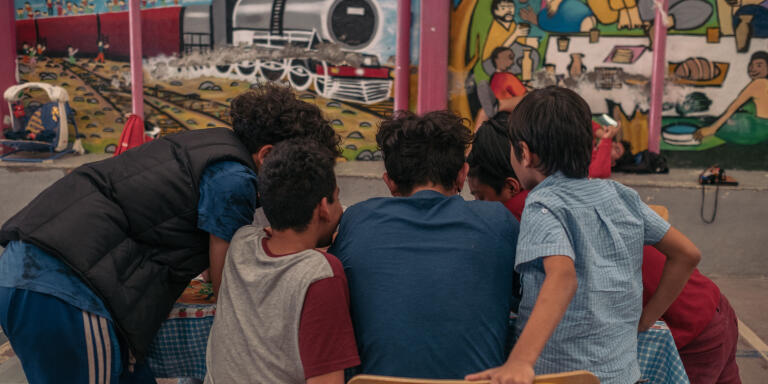 Des enfants migrants regardent une video sur le smartphone de l' un d'eux dans la cour du refuge pour migrants Cafemin. 28/04/2021 Mexico, CDMX, Mexique.