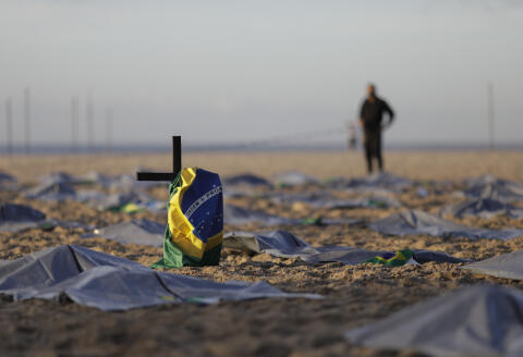 A Brazilian flag hangs on a cross amid mock body bags on Copacabana beach placed by the NGO "Rio de Paz" in memory of the 400,000 victims of COVID-19 nationwide in Brazil, in Rio de Janeiro, Brazil, Friday, April 30, 2021. (AP Photo/Silvia Izquierdo)