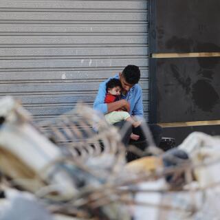 A Palestinian man holds his son as he sits outside a closed shop in front of his destroyed home in a residential neighbourhood in Gaza City early on May 16, 2021, following massive Israeli bombardment of the Hamas-controlled enclave. The previous day, an Israeli air strike flattened a 13-floor building housing Qatar-based Al Jazeera television and the US news agency the Associated Press in the Gaza Strip.  / AFP / MOHAMMED ABED
