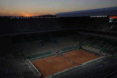 United States's Tennys Sandgren, left serves to Serbia's Novak Djokovic during their first round match in an almost deserted Philippe Chatrier stadium as the sun sets on day three of the French Open tennis tournament at Roland Garros in Paris, France, Tuesday, June 1, 2021. Spectators are not allowed in the stadium after the curfew of 2100, due to the on going coronavirus pandemic. (AP Photo/Christophe Ena)
