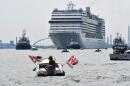 An environmental protesters from the "No Grandi Navi" group (L), demonstrates aboard a small boat against the presence of cruise ships in the lagoon, as the MSC Orchestra cruise ship (Rear) leaves Venice across the basin on June 05, 2021. The cruise ship, which arrived in Venice on June 03, 2021 for the first time in 17 months, signalling the return of tourists after the coronavirus pandemic but enraging those who decry the impact of the giant floating hotels on the world heritage site, picked up about 650 passengers on June 05, before heading south to sample the delights of Bari, Corfu, Mykonos and Dubrovnik. / AFP / MARCO SABADIN
