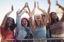 Low angle view of cheerful female fans by railing against clear sky enjoying at music festival