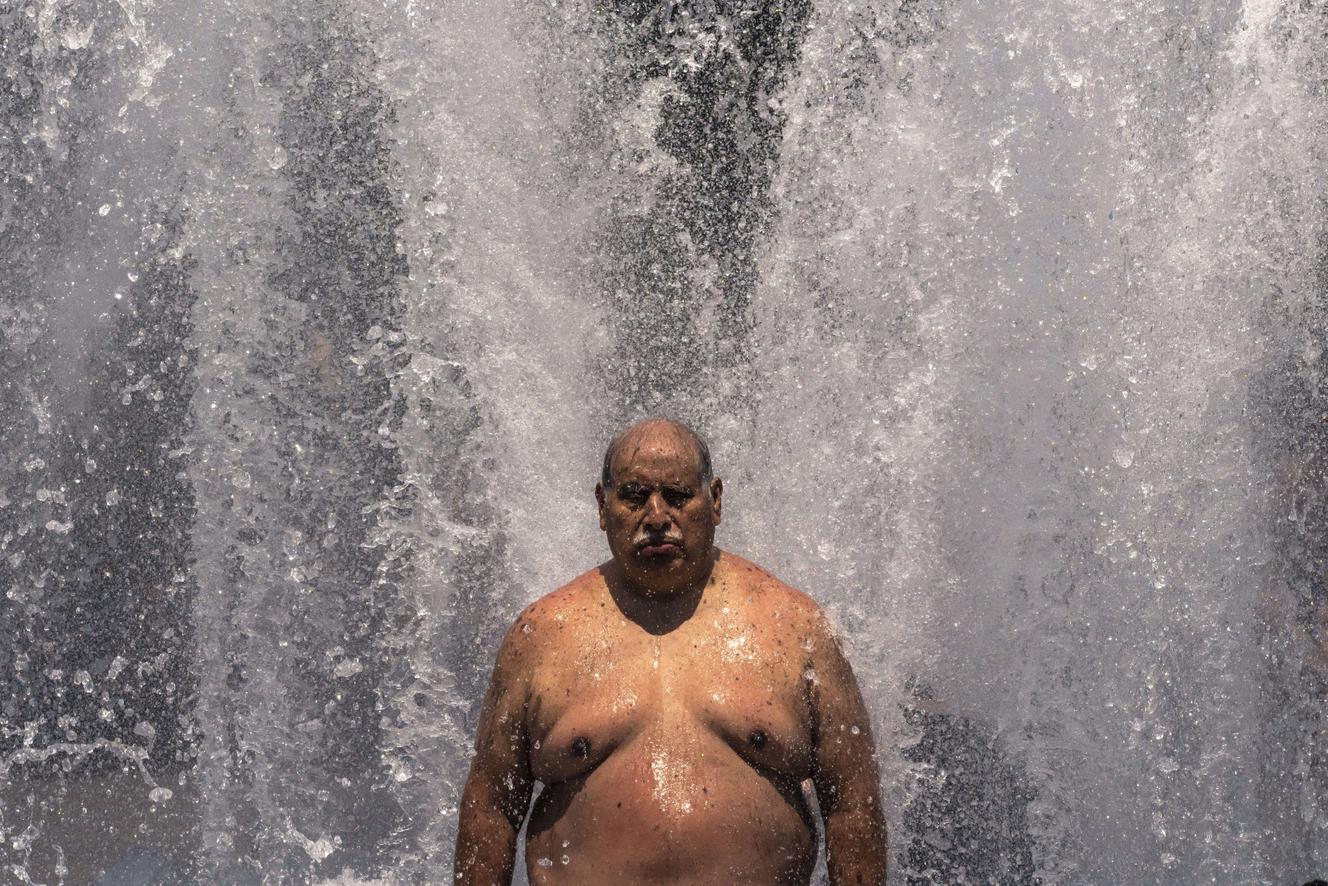 A man rests under a fountain in Portland, Oregon, June 27, 2021.