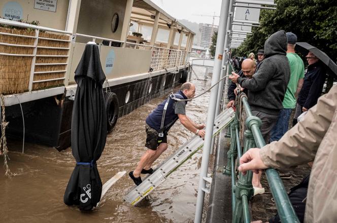 Een man daalt een ladder in het water af in een poging zijn boot te bevrijden aan de Maas in Luik, België, donderdag 15 juli 2021.