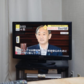 At the living of Konomi's home with TV news about Tokyo Olympic.. 
The man in a screen is a prime minister, Yoshihide Suga.