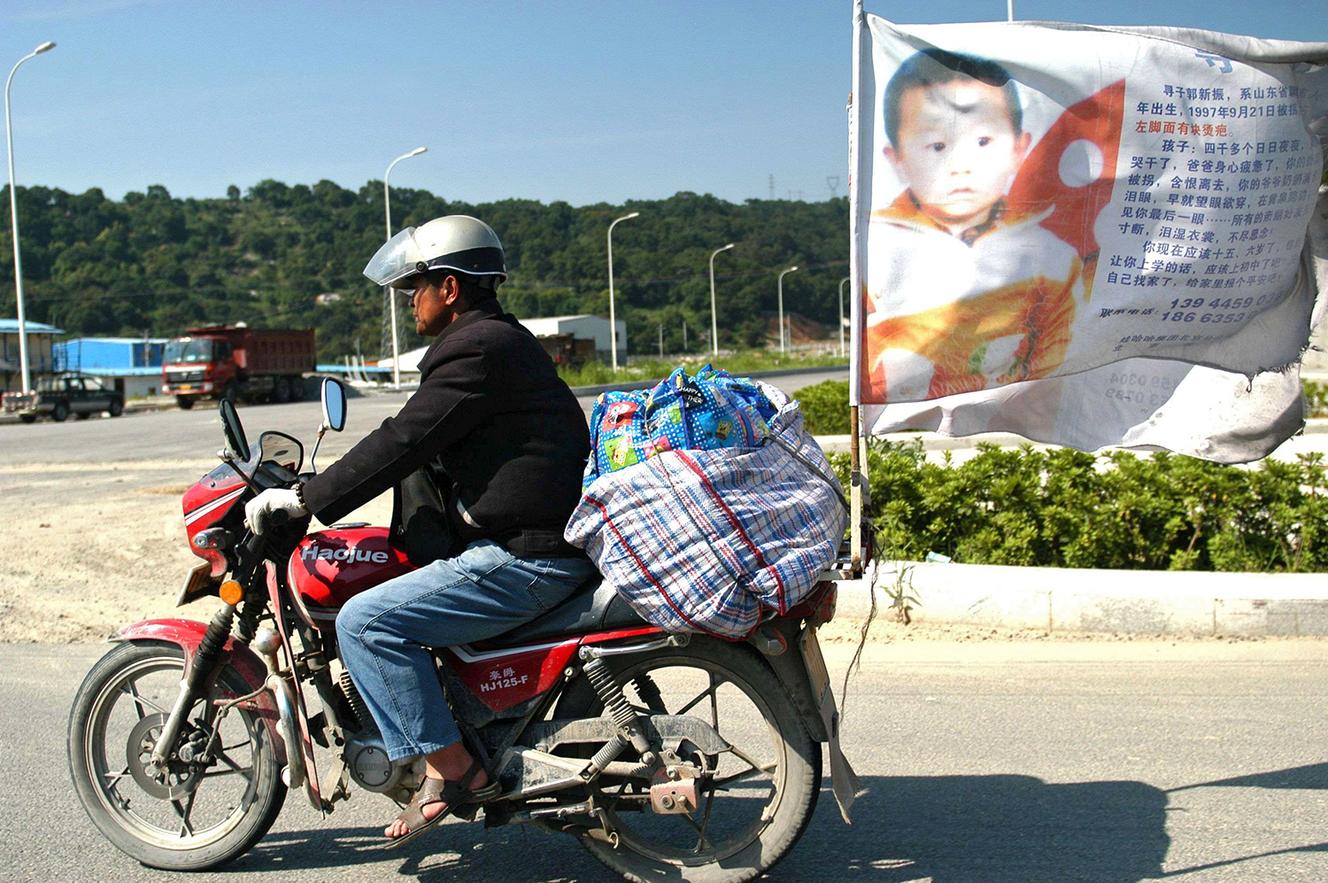 Guo Gangtang, 51 ans, a passé vingt-quatre ans à chercher son fils. Il est ici sur sa moto équipée de bannières (dans le Shandong, en 2010).