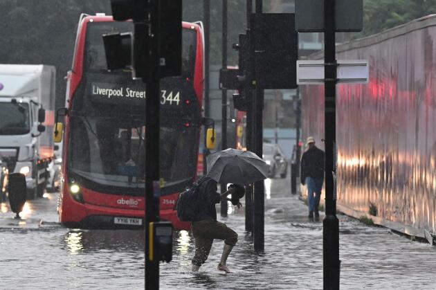 Ein Fußgänger überquert am 25. Juli 2021 in London vor einem Bus der öffentlichen Verkehrsmittel eine überflutete Straße.