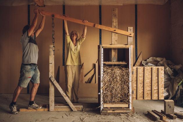 Hervé Callo et Catherine Jouanic dans leur futur appartement, actionnent la presse à paille (qu’ils ont eux-même fabriquée) pour l'isolation des murs. Riec-sur-Bélon (Finistère), le 14 septembre 2021.