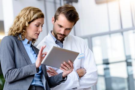 Erfahrene Geschäftsfrau  aus Verwaltung oder Pharmaindustrie mit Tablet in der Hand bespricht mit Arzt in Krankenhaus bei Meeting Ergebnisse oder Diagnose, Deutschland, Bayern, München