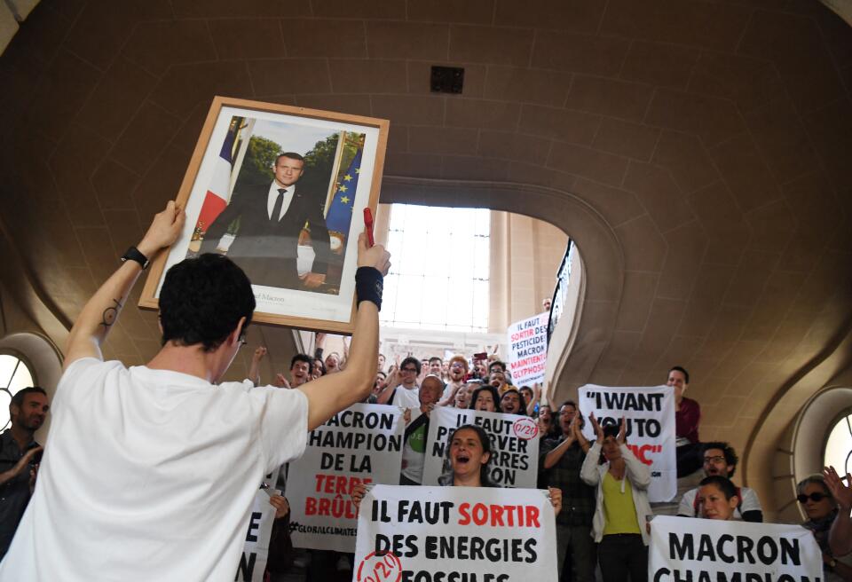 A young man shows a portrait of French President Emmanuel Macron he removed from a wall of a city hall while others hold plackards against climate change during a 'Fridays'for climate' protest in Paris on May 24, 2019 part of the worldwide youth campaign ahead of the EU elections. - (Photo by Alain JOCARD / AFP)