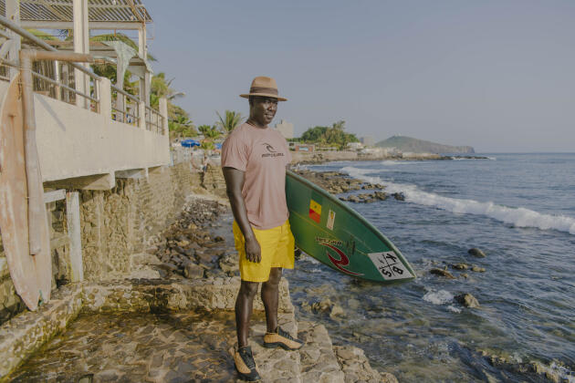 Oumar Sèye, ancien surfeur professionnel et gérant d’une entreprise spécialisée dans le surf, pose avec sa planche sur la plage des Almadies, à Dakar, le 19 octobre 2021.