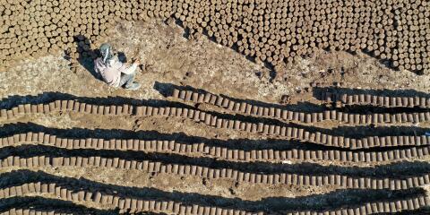 TOPSHOT - In this aerial view, a worker lines up tubes of pomace-wood, known locally as 'birin', a flammable and eco-friendly product made from olive oil waste that can be used to heat houses during winter, at factory in the town of Armanaz, in the northwestern part of Syria's Idlib province, on October 16, 2021. The waste that remains after the olives are pressed to make oil, is gathered, shaped in to pipes, cut and then sun dried. (Photo by OMAR HAJ KADOUR / AFP)