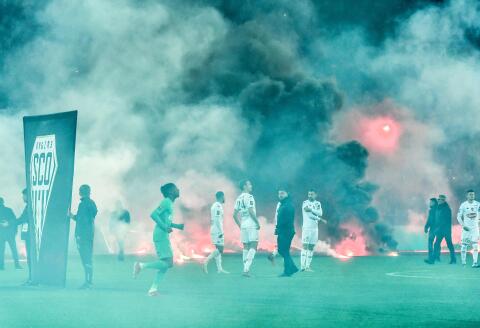 AS Saint-Etienne and SCO Angers football players react on the pitch after AS Saint-Etienne supporters launched smoke canisters to protest against the last place of their football club in the ranking of the French L1 championship, prior to the start of the French L1 football match between AS Saint-Etienne and SCO Angers at the Geoffroy Guichard stadium in Saint-Etienne, central France, on October 22, 2021. Incidents broke out during the pre-match protocol Saint-Etienne/Angers of the 11th day of Ligue 1, caused by the ultras groups of the club stéphanois, and the kickoff of the game scheduled for 21:00 has been delayed. (Photo by PHILIPPE DESMAZES / AFP)
