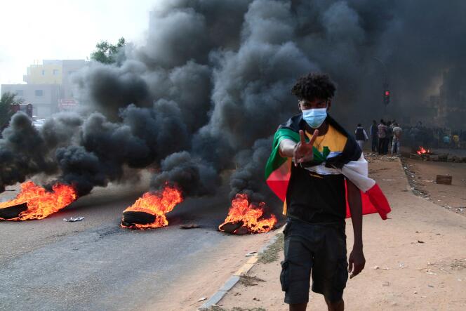 Un manifestant soudanais drapé du drapeau national à côté de pneus en feu lors d’une manifestation dans la capitale Khartoum, le 25 octobre 2021.