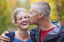 Husband Gives Wife A Kiss On The Cheek While Walking Down A Park Path In Autumn; Edmonton, Alberta, Canada