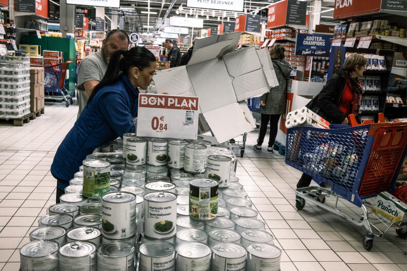 Employees unpack cans of food as a customer fills her shopping cart in the aisle of a hypermarket in Givors near Lyon on March 13, 2020, during the COVID-19 outbreak caused by the novel coronavirus. - With the acceleration of the contamination in France, the date of March 12, 2020 was a turning point, as the French President announced that all schools would be closed until further notice, and called on elderly people to stay home as much as possible. (Photo by JEAN-PHILIPPE KSIAZEK / AFP)