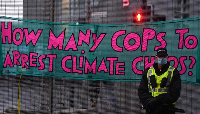 Un policier surveille une manifestation. Derrière lui, sur la banderole est écrit : « Combien de flics pour arrêter le chaos climatique ? »