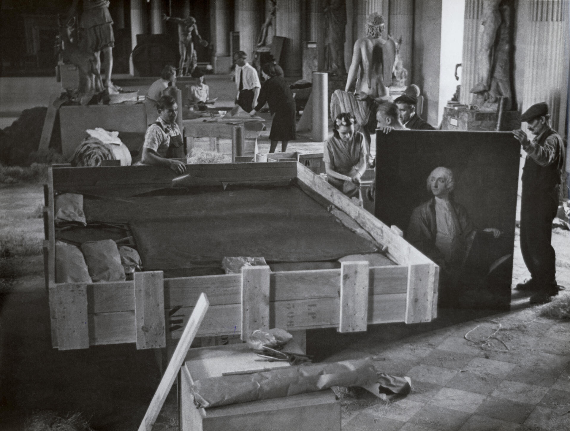 Dans la salle des Cariatides du Louvre, les tableaux sont entassés dans des caisses avant leur évacuation. Chaque toile est isolée par du papier huilé et de la ouatine. A Paris, à la fin de l’été 1939.