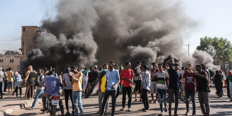 Des manifestantes soudanais se tiennent à côté de la fumée qui s'eleve à la suite des pneus en feu  pendant une manifestation dans le quartier d'Al-Sahafa à Khartoum le le 25 novembre 2021.