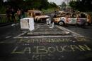 TOPSHOT - People walk past a road block made of burnt vehicles and debris and an inscription on the road reading in French "The Republic of La Boucan" at the cut-off locality of La Boucan in Sainte-Rose, in the French Caribbean island of Guadeloupe on November 30, 2021, as France's minister for overseas territories left Guadeloupe at an impasse over ways to end more than a week of violent protests sparked by Covid-19 restrictions. Unrest in the former colonial outpost began with a protest over compulsory Covid-19 vaccinations for health workers, but quickly ballooned into a broader revolt over living conditions, and spread to next door Martinique. (Photo by Christophe ARCHAMBAULT / AFP)