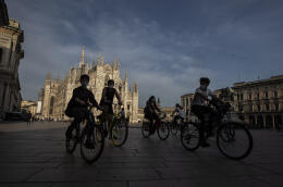 People bike in front of the Duomo gothic cathedral in Milan, Italy, Monday, May 18, 2020. . On Monday, Italians enjoyed a first day of regained freedoms, including being able to sit down at a cafe or restaurant, shop in all retail stores or attend church services such as Mass. (AP Photo/Luca Bruno)