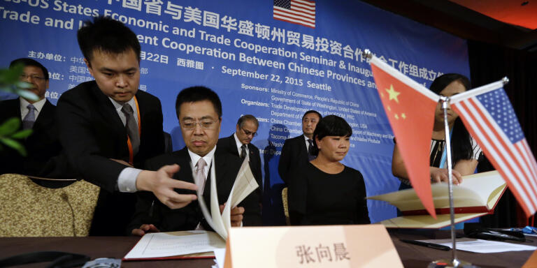 Zhang Xiangchen, seated left, Deputy China International Trade Representative, and Joby Shimomura, seated right, Chief of Staff for Gov. Jay Inslee, are handed documents during a signing ceremony at a U.S. Trade and Investment Cooperation Conference Tuesday, Sept. 22, 2015, in Seattle. The Ministry of Commerce of China (MOFCOM), the State of Washington and partners hosted the conference to explore cooperation between Chinese provinces and U.S. businesses. (AP Photo/Elaine Thompson)