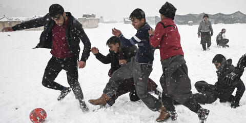 Youths play football during heavy snowfall in Kabul on January 4, 2022. (Photo by Mohd RASFAN / AFP)