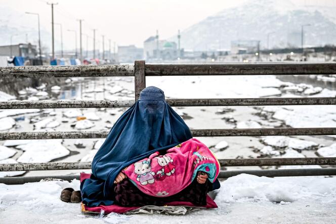 Une Afghane vêtue d’une burqa demande l’aumône aux passants sur un pont couvert de neige à Kaboul, le 6 janvier 2022.