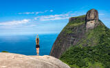 Beautiful image from above of Pedra Bonita overlooking the Pedra da Gávea with girl in yoga position contemplating a blue sky and sea background on Rio de Janeiro Brazil; Shutterstock ID 1384112000; to: -; dp: -