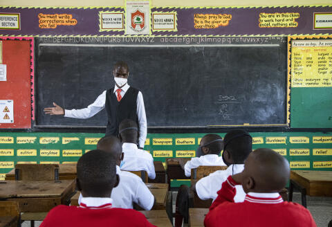 A teacher welcomes back students during a classroom lesson on day one of re-opening schools in Kampala, Uganda on January 10, 2022. - Uganda's Health Minister, Dr Jane Ruth Aceng, announced last week that Uganda is now in the third wave of a pandemic that has no end in sight. (Photo by Badru KATUMBA / AFP)