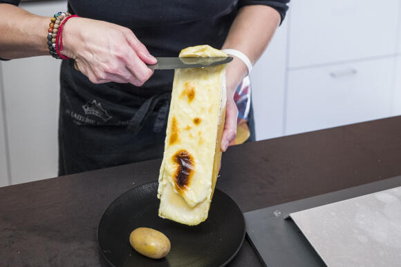 13/01/2022 - Suisse / Orsières - Sabine Darbellay, responsable des ventes de la laiterie d'Orsières, racle soigneusement une portion de fromage fondu depuis une demi-meule chauffée sous un four à raclette. Matthieu Zellweger / HAYTHAM PICTURES