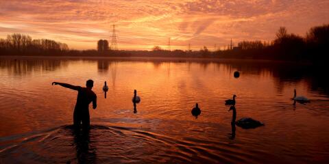 A man walks into the water as the sun rises over Sale Water Park in Manchester, Britain, January 18, 2022. REUTERS/Phil Noble