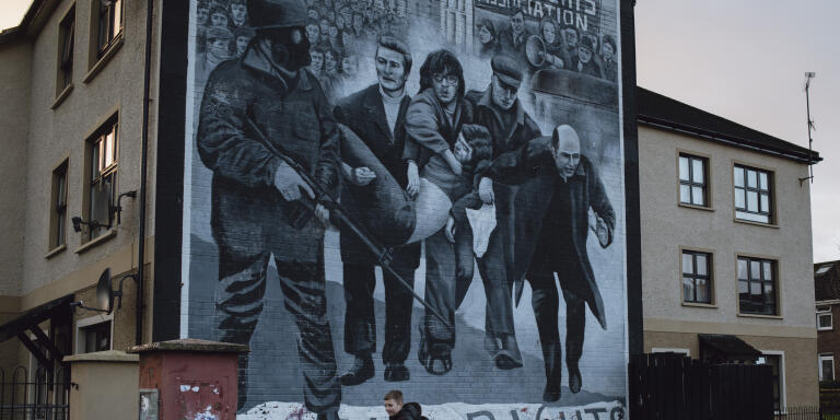 Two boys ride a scooter underneath a mural in the Bogside neighbourhood of Derry, Northern Ireland, on January 11, 2022.
The mural depicts a scene from Bloody Sunday, where a group of men, including a local Catholic priest, carrying the body of Jack Duddy from where he was shot.
On 30 January 1972, 14 people were killed by the British Army in the province's second largest city, during a civil rights demonstration. 

Philip Hatcher-Moore for Le Monde