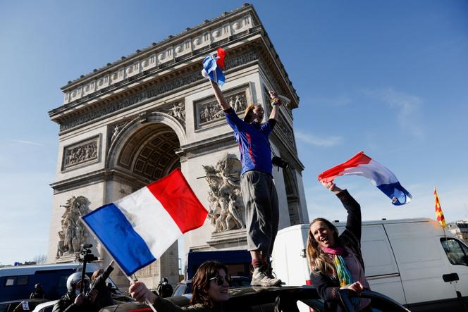 Ein Demonstrant steht am 12. Februar 2022 auf dem Dach eines Fahrzeugs, während Autos um den Arc de Triomphe in Paris herumfahren.