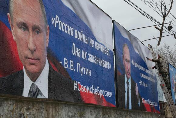 Un homme finit de coller d’immenses pancartes à l’effigie du président russe, Vladimir Poutine, sur lesquelles on peut lire « La Russie ne commence pas les guerres, elle les termine » (à gauche) et « Nous viserons la démilitarisation et la dénazification de l’Ukraine » dans le centre-ville de Simferopol, en Crimée, le 4 mars 2022.