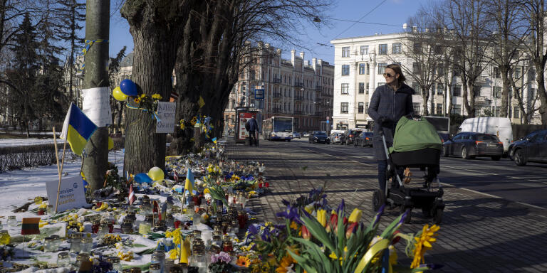 Sur le boulevard Kalpaka à Riga, Lettonie, entre l’ambassade d’Ukraine et celle de la Russie, séparées par seulement quelques centaines de mètres, des milliers de bougies, d’affiches, de fleurs et de marques de soutien à l’Ukraine et contre la guerre ont été déposés tous le long du boulevard. Une femme marche avec sa poussette le long du boulevard et regarde les hommages déposés, le 9 mars 2022.