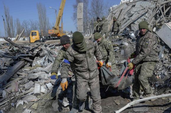 Des soldats ukrainiens portent un soldat mort à travers les débris de l'école militaire touchée par des roquettes russes la veille, à Mykolaïv, dans le sud de l'Ukraine, le 19 mars 2022.