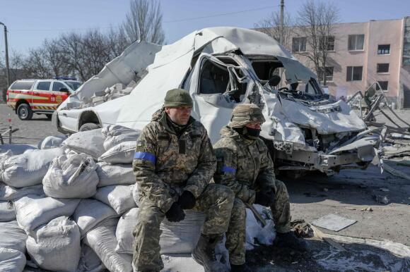 Des soldats ukrainiens sont assis à côté de l'école militaire touchée par des roquettes russes la veille, à Mykolaïv, dans le sud de l'Ukraine, le 19 mars 2022.