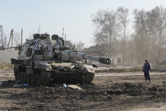 Un habitant regarde un char russe endommagé dans la ville de Trostsyanets, à quelque 400 km à l'est de la capitale Kiev, en Ukraine, lundi 28 mars 2022.