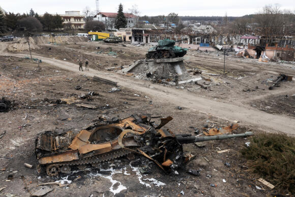 Des habitants passent devant un char russe endommagé dans la ville de Trostianets, à l’est de la capitale, Kiev, en Ukraine, lundi 28 mars 2022. Un monument de la seconde guerre mondiale est visible en arrière-plan.