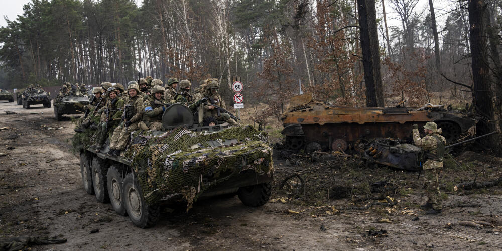 Des soldats ukrainiens sur un blindé passent devant un tank russe détruit, dans les faubourgs de Kiev, en Ukraine, le 22 mars 2022.