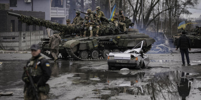 A man stands next to a civilian vehicle that was destroyed during fighting between Ukrainian and Russian forces that still contains the body of the driver as Ukrainian servicemen ride past on a tank outside Kyiv, Ukraine, Saturday, April 2, 2022. As Russian forces pull back from Ukraine's capital region, retreating troops are creating a 