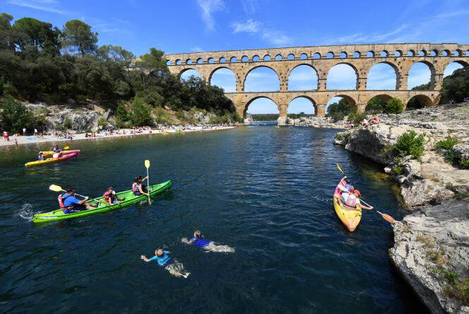 Tourists swim in the Gard river and sail in kayaks in front of the Pont du Gard on August 21, 2019 in Vers-Pont-du-Gard, southern France.