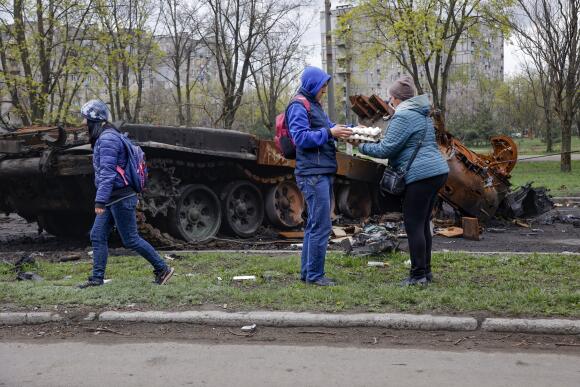 Des résidents de Marioupol vendent des œufs sur un marché de rue improvisé près d'un véhicule militaire endommagé, dans une zone contrôlée par les forces séparatistes soutenues par la Russie, vendredi 22 avril 2022.
