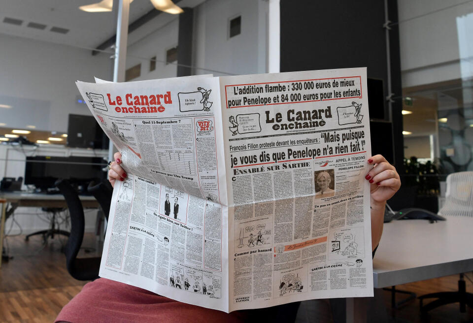 This picture taken on February 1, 2017 in Paris shows a journalist reading the February 1, 2017 issue of French satirical newspaper "Le Canard Enchaine", with a headline relating to French presidential election candidate for the right-wing Les Republicains (LR) party Francois Fillon allegedly giving his wife fake jobs and reading "Francois Fillon protests in front of investigators: "But since I tell Penelope didn't do anything!"". - Fillon on February 1 hit back at fresh claims he paid his family huge sums for doing "fake jobs", accusing the incumbent Socialist government of mounting what he called an "institutional coup d'etat". The scandal, which first erupted last week, is pulling down Fillon's campaign, with a new poll showing that the former PM, who for weeks was the frontrunner in the race, would now be eliminated in the first round of the election in April. The Canard Enchaine newspaper reported on February 1, 2017 that Fillon had arranged for his wife Penelope to be paid around 830,000 euros ($900,000) as a parliamentary aide for more than a decade. (Photo by CHRISTOPHE ARCHAMBAULT / AFP)