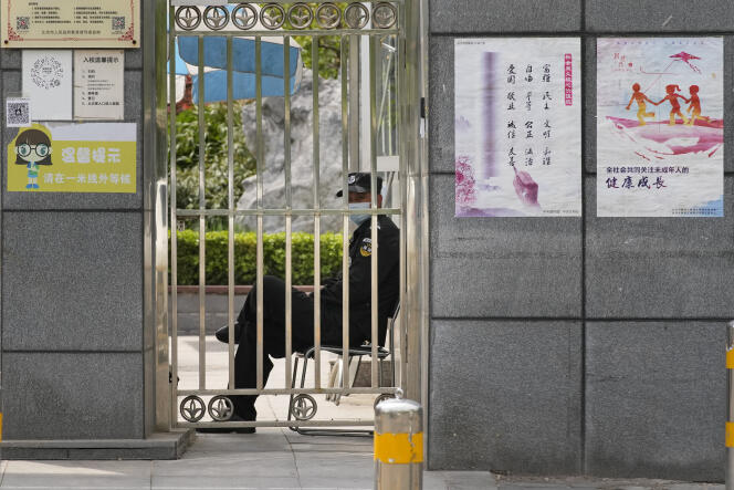 A security guard looks out from a closed gate outside a school on Thursday, April 28, 2022, in Beijing.