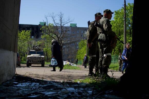Des habitants marchent dans la ville de Marioupol alors que les militaires de la « république populaire de Donetsk » autoproclamée gardent une zone, le 29 avril 2022.